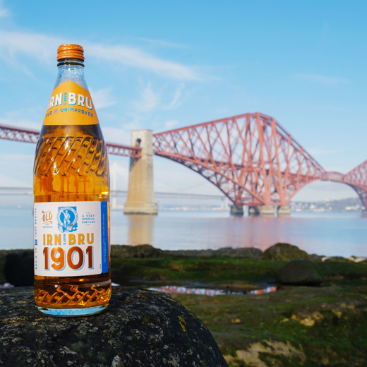 A glass bottle of IRN-BRU 1901 with the Forth Railway Bridge in the background. 
